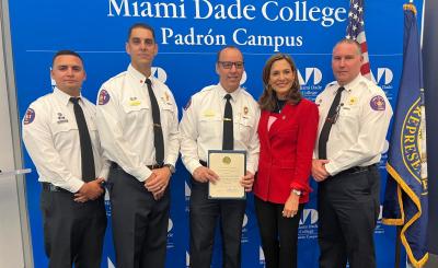 Three firefighters in uniform stand next to Congresswoman Maria Elvira Salazar holding an award.